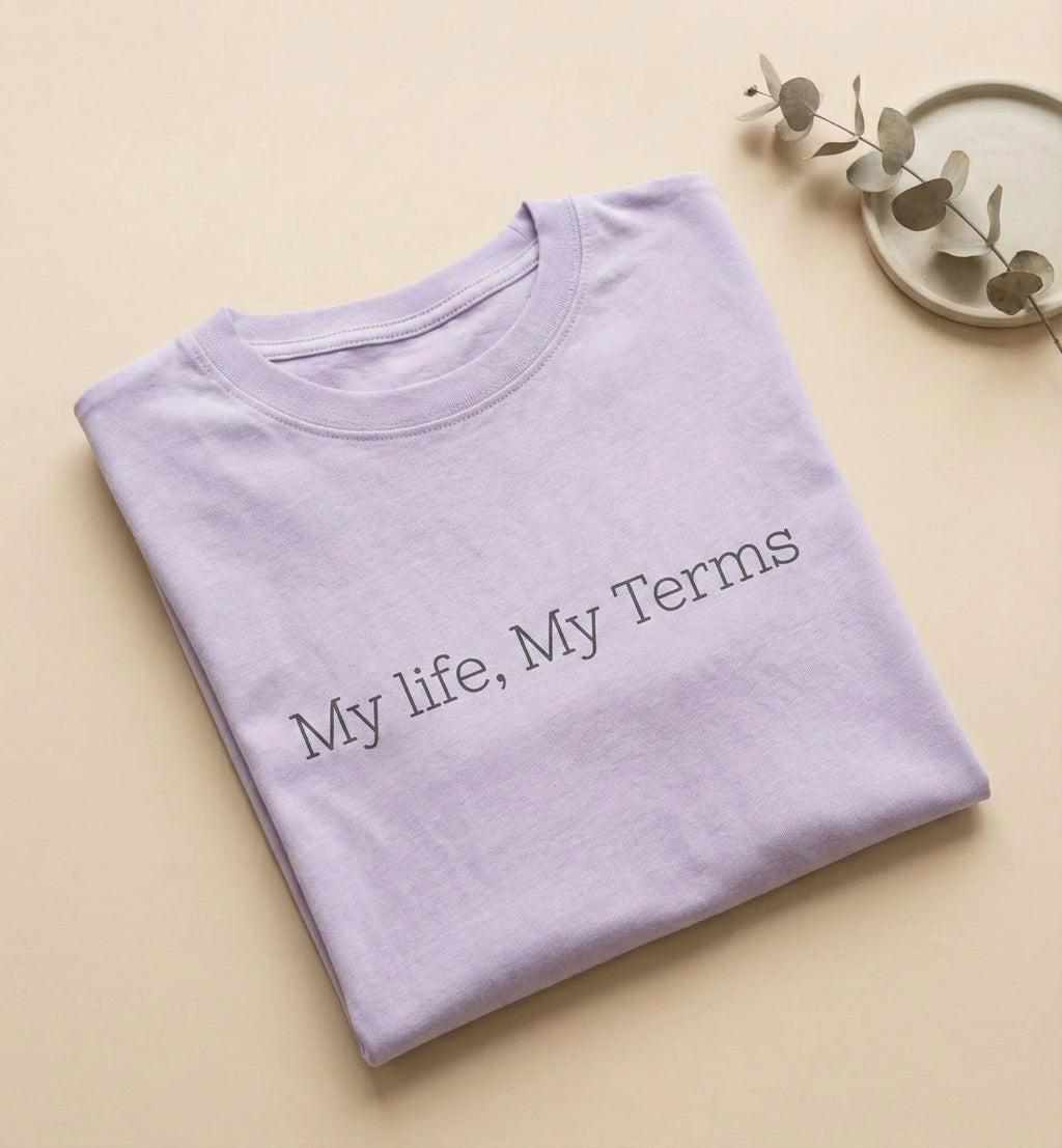 Folded purple shirt with 'My life, My Terms' text on a beige background