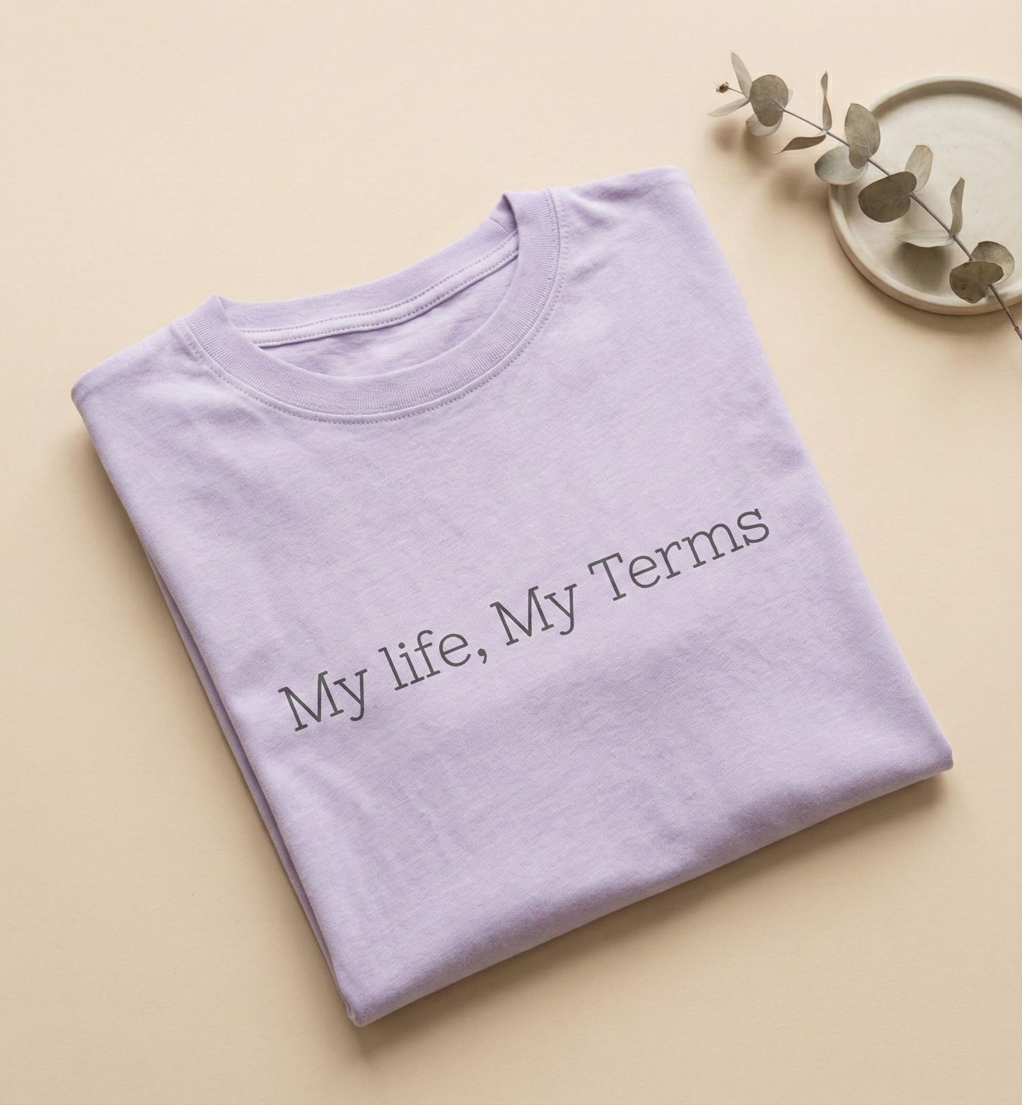 Folded purple shirt with 'My life, My Terms' text on a beige background