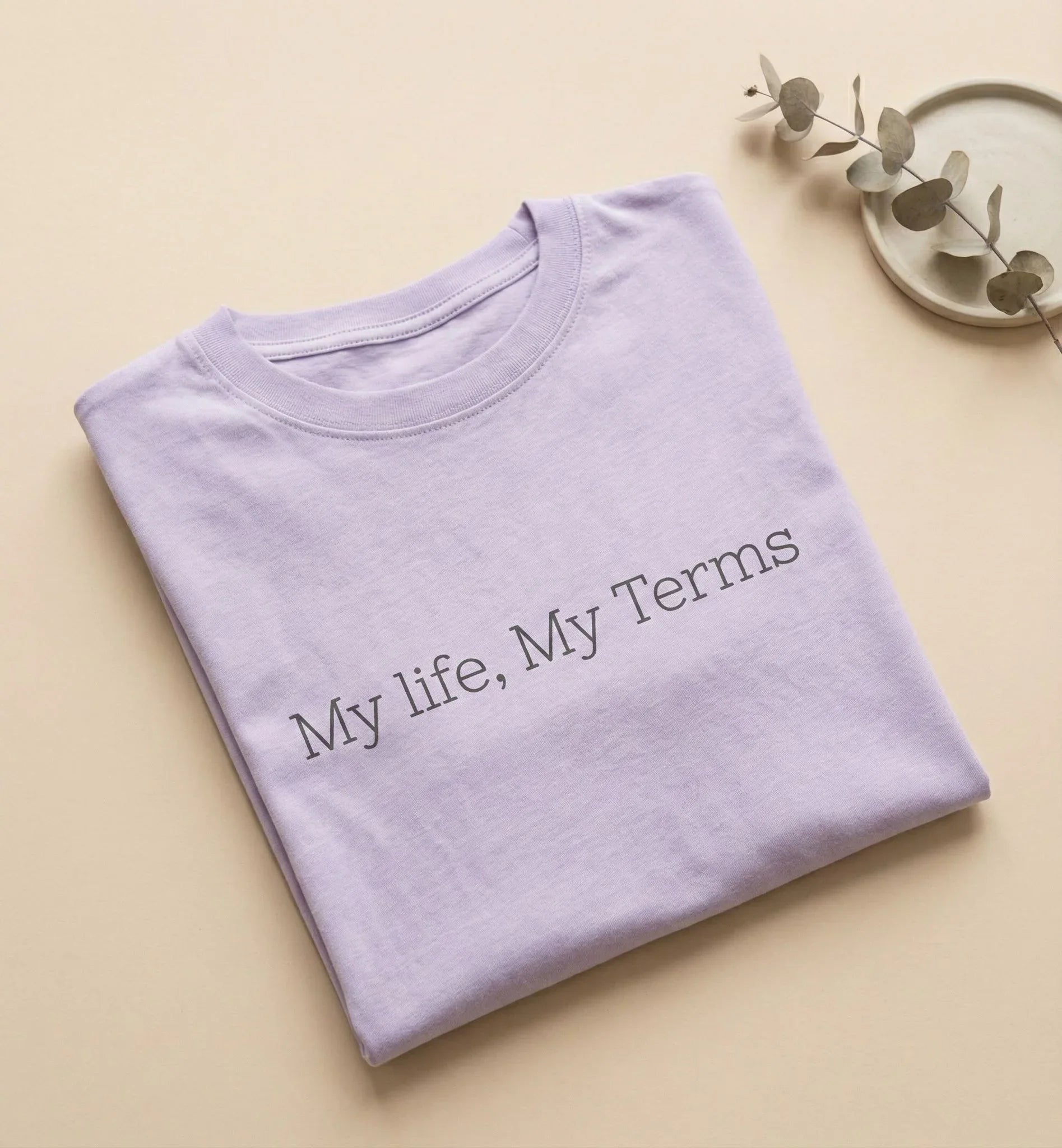 Folded purple shirt with 'My life, My Terms' text on a beige background